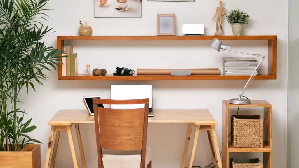 Empty wooden office desk with laptop and digital tablet on it with comfortable chair and designed shelf on the wall