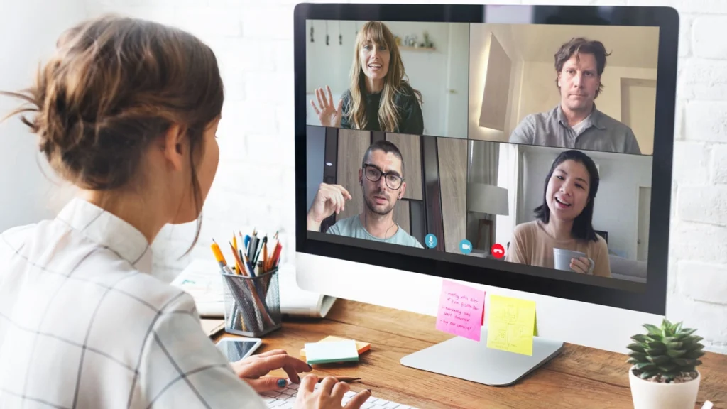 A woman sits at a desk, engaged in a video conference on her computer screen.