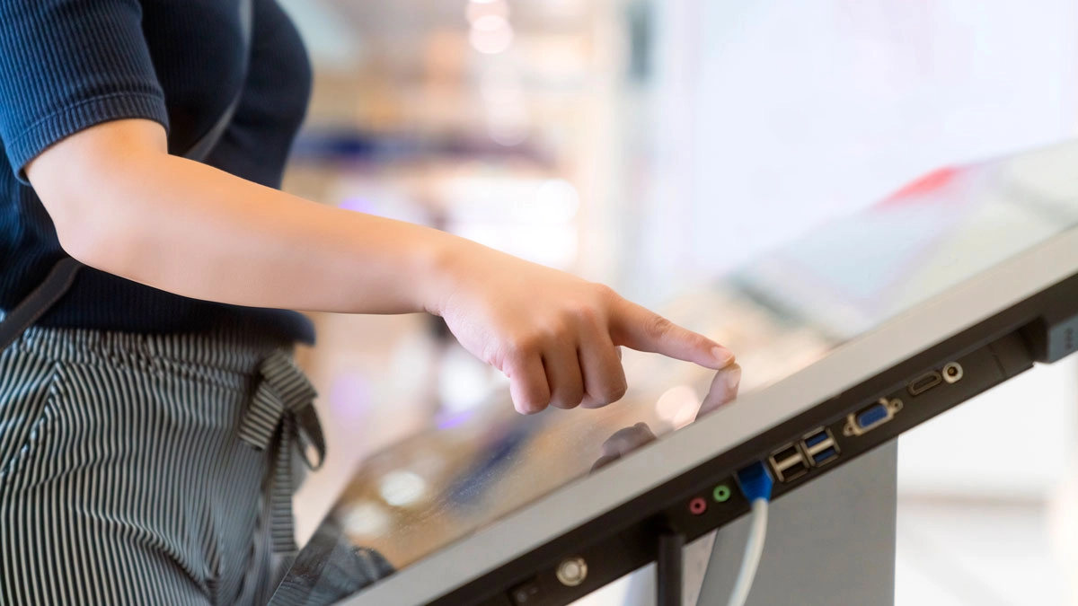 A person points at a touch screen, indicating interaction or selection on the device.