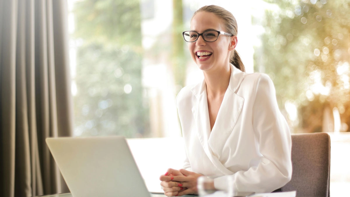 A smiling woman in glasses sits at a table with a laptop, representing a positive business environment for AV solutions.